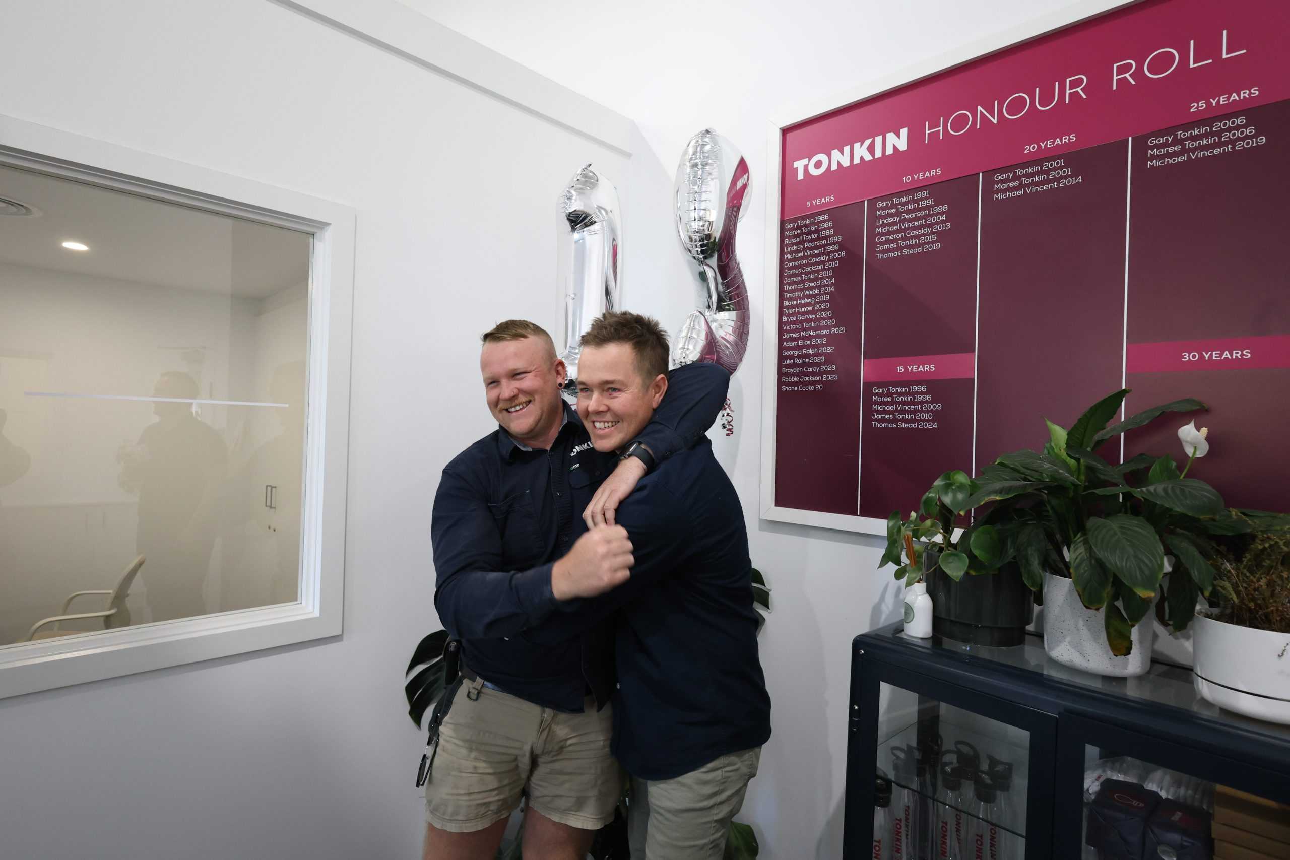 Two Tonkin Group employees celebrating in front of the Tonkin Roll of Honour.